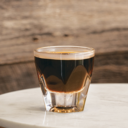Glass of cold brew being served hot in tumbler on marble tabletop